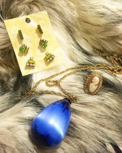 Picture of blue necklace, three sets of green earrings, and a vintage ring against a fur background