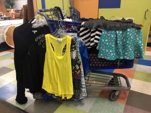 A Goodwill cart filled with clothing items with shirts and skirts hanging on the side