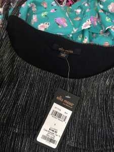 A picture of the tag of a black and grey ella moss shirt sitting atop a blue floral clothing item
