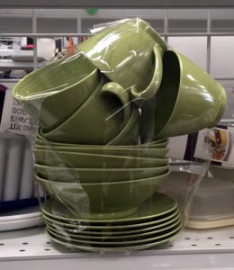 A stack of olive green plates, saucers, and tea cups on a shelf at Goodwill