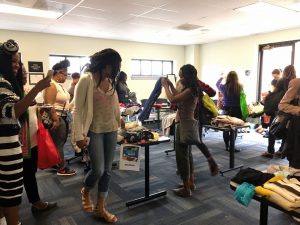 A picture of the DCGF Swap attendees looking through the items that are being swapped. Most of the items are clothing and are placed on table.