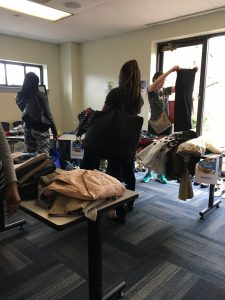 A picture of the DCGF Swap attendees looking through the items that are being swapped. Most of the items are clothing and are placed on tables and on racks