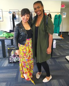 A picture of two women: the DCGF in a floral long skirt and leather jacket and a second woman in a long dark green jacket, black pants, and black shirt