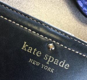 A gold Kate Spade New York logo on a purse (closeup of the logo itself)