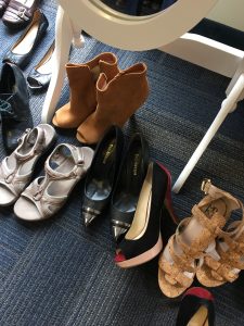 A picture of multiple pairs of shoes: a tan pair of short heel boots, silver sandals, black heels, and tan sandal heels 