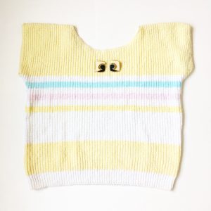 A picture of a sleeveless striped sweater that is a pale yellow, blue, pink, and white. On top of the sweater is a pair of artsy, stud, black and cream earrings with gold outlining