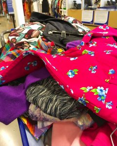 A picture of a shopping cart filled the the brim with colorful Goodwill items with the interior of the Clinton Goodwill retail store in the background