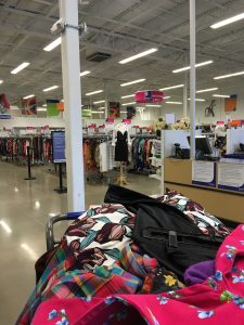 A picture of a shopping cart filled the the brim with colorful Goodwill items with the interior of the Clinton Goodwill retail store in the background