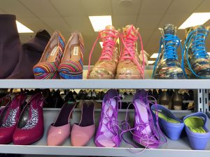 A picture of different kinds of colorful shoes at the Waldorf Goodwill of Greater Washington retail location. These include pink heels, two pairs of boots, one with pink laces and the other with blue, multicolored heels, and purple heels