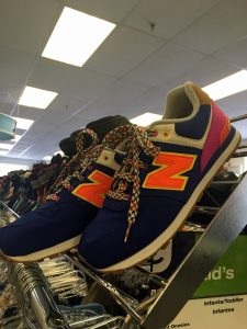 A picture of New Balance shoes, the primary color is dark blue, the N logo is a bright orange, and the heel is purple