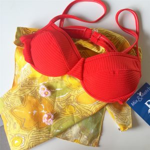 A picture of a woman's red bathing suit top laying on a yellow floral patterned napkins