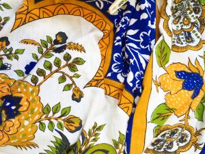 A table cloth with an ornate blue, white, and gold pattern with a print of a plant on it