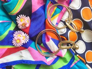 A pair of gold, dangle, hoop earrings and pink flower stud earrings on top of colorful patterned scarves 