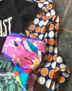 A picture of two colorful, patterned, vintage scarves (pink with different shapes and blue with orange and white dots) and the corner of a black, Everlast crop top shirt and a pair of green and blue patterned high wasted shorts
