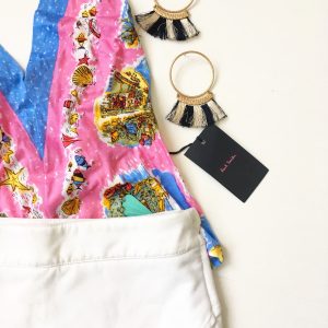 A picture of a pink holter top with beach prints on it; a white skort, and a pair of hoop earrings that have black and white tassels on them 