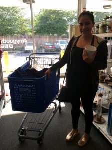 A picture of a woman in black shopping next to a blue Goodwill of Greater Washington shopping cart. She is holding a white mug