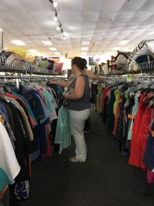 A woman in white pants and a sleeveless shirt shopping the racks at the Alexandria Goodwill of Greater Washington retail store