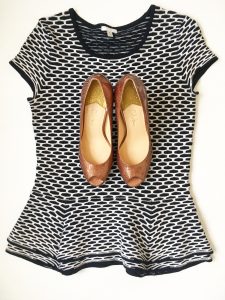 A picture of a top that is a stretchy, black and white, short sleeved, peplum blouse by Intermix in a size medium. On top of the shirt is a pair of reddish, warm gold, metallic, short, open-toed, modern, Cole Haan heels in a size 7