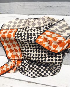 A vintage silk scarf with a black, white, and orange houndstooth patter on it laying on a set of white stairs