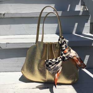 A picture of a gold purse with a vintage silk scarf with a black, white, and orange houndstooth pattern on it tied around one of the handles of the purse