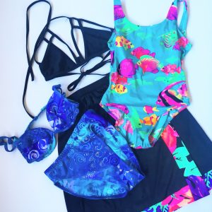 A picture of a blue, high waisted bikini with different 90's patterns on it, a one piece bathing suit that is a turquoise color with hot pink tropical fish on it, and a black bikini top and a black skirt with a pastel boarder.