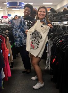 A picture of two women, the Caucasian woman in front is holding a Harry Potter tank top and the African American woman behind her is holding a blue and white patterned tank top 