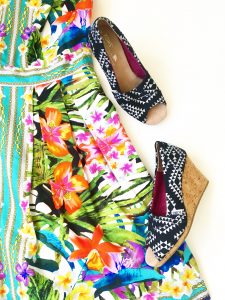 A close up of the pair of black and white Aztec triangle patterned TOMS wedge open toed shoes. These are next to the tropical floral patterned Maggy London dress