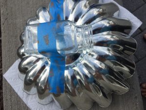 A picture of a clear salt shaker being glued to the bottom of a metal jello mold being held in place by blue painters tape