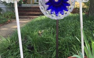 A picture of some cut broom handles acting as stems for DIY flowers in front of a yard in front of a yellow house