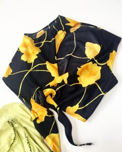 A black crop top with yellow flowers on it. It has a sheen and ties in the back