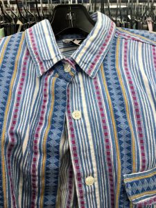 A picture of a vintage, 1990's, button up top. It has a few shades of blue and pink and has vertical stripes in different patterns. This is a close up of the buttons and collar