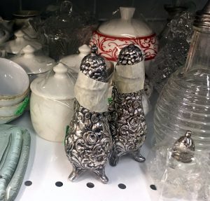 A picture of two pewter salt and pepper shakers with flowers carved into them with various other kitchen containers in the background