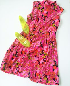 A pink, floral, sleeveless dress with a pair of green jelly flat shoes