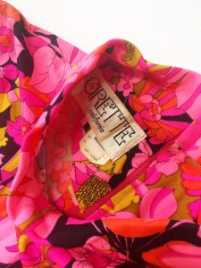 A pink, floral, sleeveless dress with a pair of green jelly flat shoes. This picture is a close up of the tag