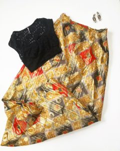 A picture of three items: a black shirt, a pair of black, geometric crystal earrings, and a metallic gold, black, and red patterned material and lined with a cream fabric maxi dress