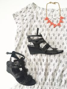 A picture of a white Joie day dress. It has a small, black, design all over it in rows that almost look like small bird's feet. The dress has very short sleeves and gets smaller around the waist. Also pictured is an orange necklace with rine stones. Also pictured is a pair of black, wedge sandals. 