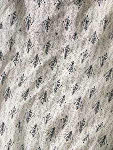 A close up of the pattern of the white Joie day dress. It has a small, black, design all over it in rows that almost look like small bird's feet. The dress has very short sleeves and gets smaller around the waist.