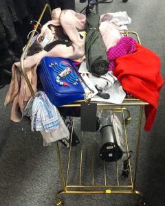 A brass bar cart painted gold covered in various items ranging from a blue purse to various women's tops