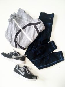 A picture of three objects: a grey Lululemon zip up jacket with a blue stripe through the middle of it, a pair of Lululemon blue workout pants, and a pair of Nike grey and black sneakers