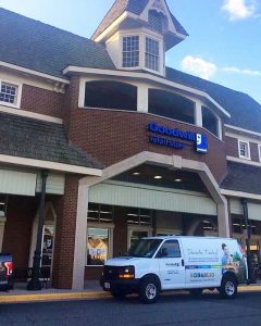 The storefront of the Goodwill of Greater Washington retail store and donation center located in the Sully Station Shopping Center in Centreville, VA. The Goodwill marketing van, wrapped in Goodwill branding, is parked outside the front