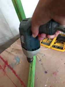 A picture of of a Black and Decker power drill drilling holes into a green frame