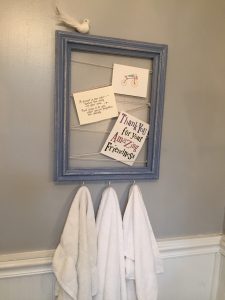 A picture of a blue frame with a twine in a zig zag pattern holding different cards and hand towels hanging from the bottom