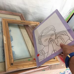 A picture of a picture of the outline of a person with their hands folded in front of their face being removed out of the back of a frame