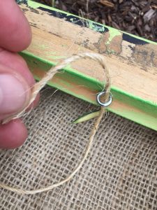 A picture of a man's hand threading a thread through an eye hook in the back of a green frame