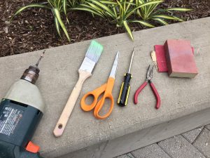 Different tools needed for the DIY frames project. These include a power drill, paint brush, scissors, a screw driver, and pliers 