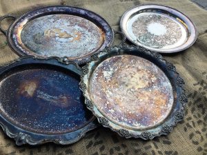A picture of four old silver serving trays. They have quite a bit of tarnish on them.