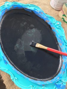 A picture of a silver serving tray that has been painted blue around the outside and is being painted with black chalkboard paint on the inside