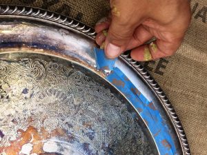 A close up of a hand applying blue painters tape to the edge of the silver tray