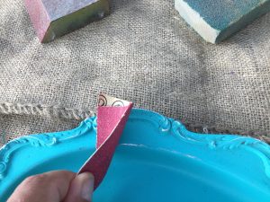 A picture of once the silver tray is painted with a couple of coats of blue paint it is then gone over lightly with sand paper to bring out the accents. The sand paper being used is red
