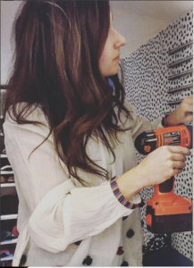 A woman with long brown hair inside the closet using a powerdrill to install different pieces to refurbish the closet.